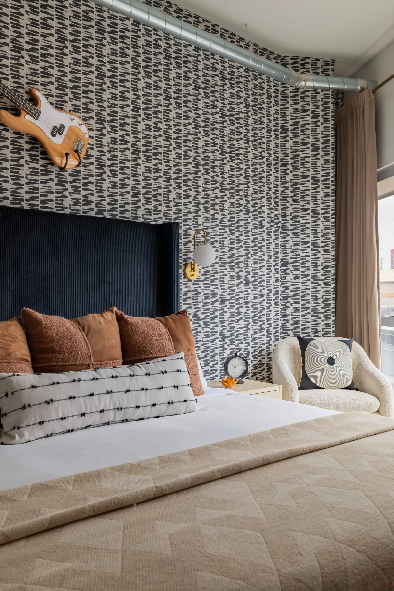 Patterned black and white wallcovering behind a navy velvet headboard with rust and striped pillows