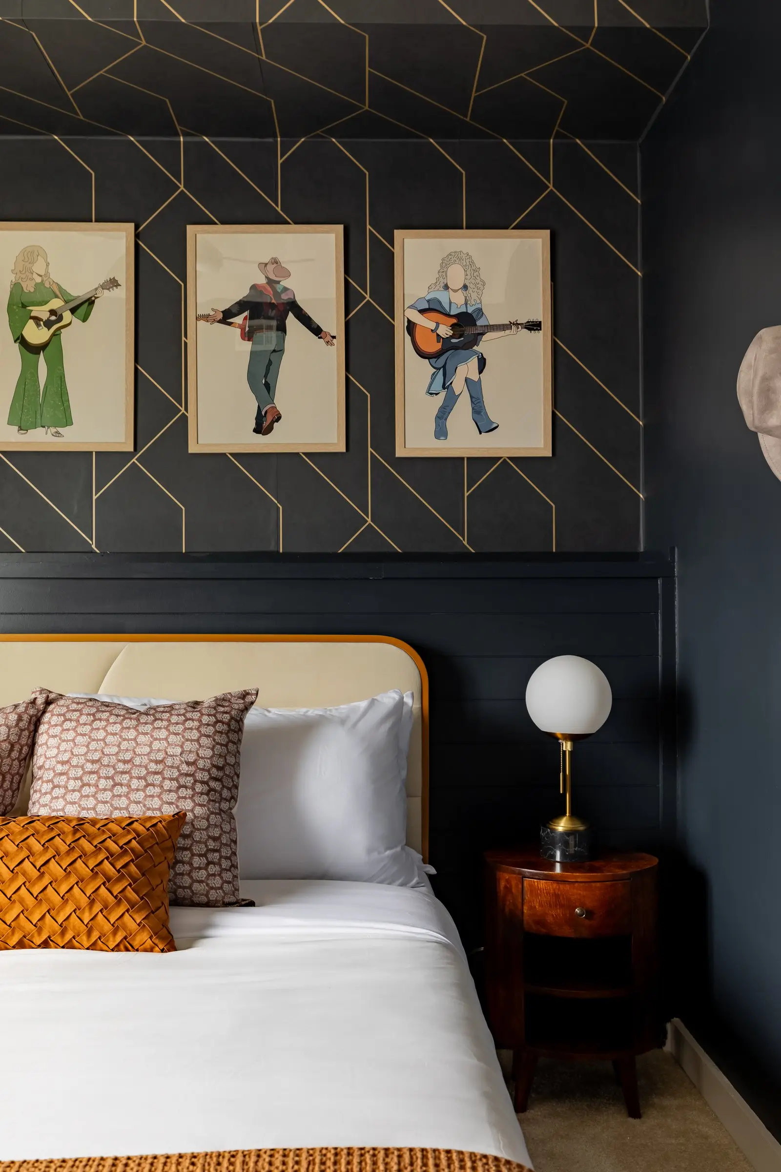 Navy bedroom with geometric gold trim, framed musician portraits and a cream upholstered headboard in a curved wood frame
