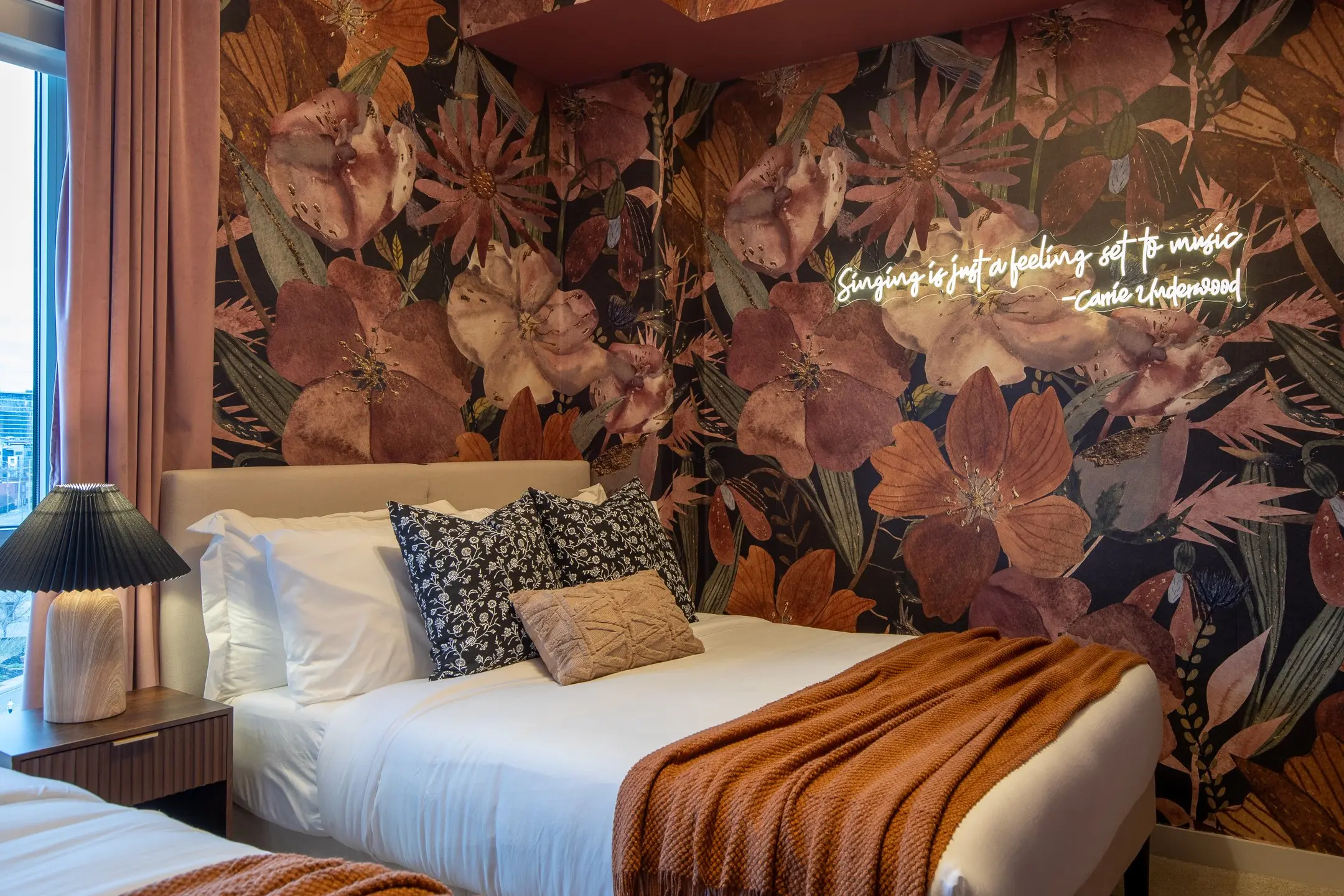 Bedroom with an oversized floral mural in plum and copper and a warm neon script sign