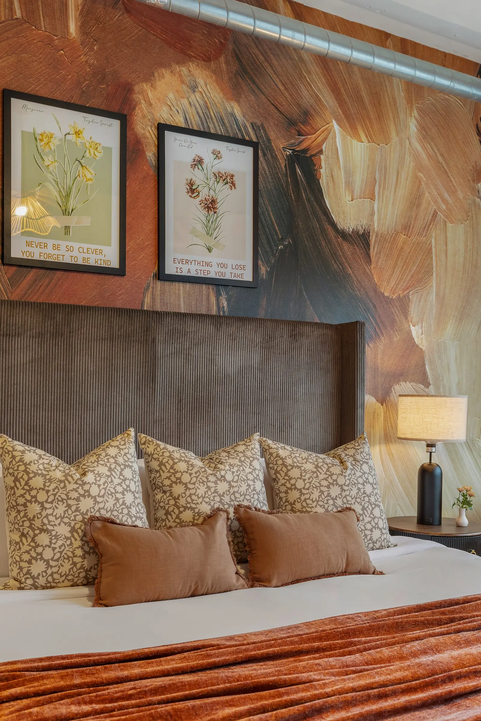 Bedroom with a painterly mural, framed botanicals and layered pillows in rust and cream