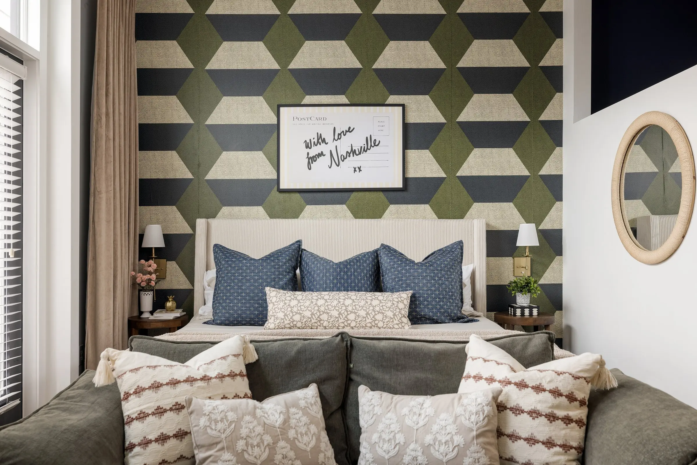 Bed in an alcove against an olive, navy and cream geometric wallcovering, with indigo pillows below a With Love from Nashville postcard print