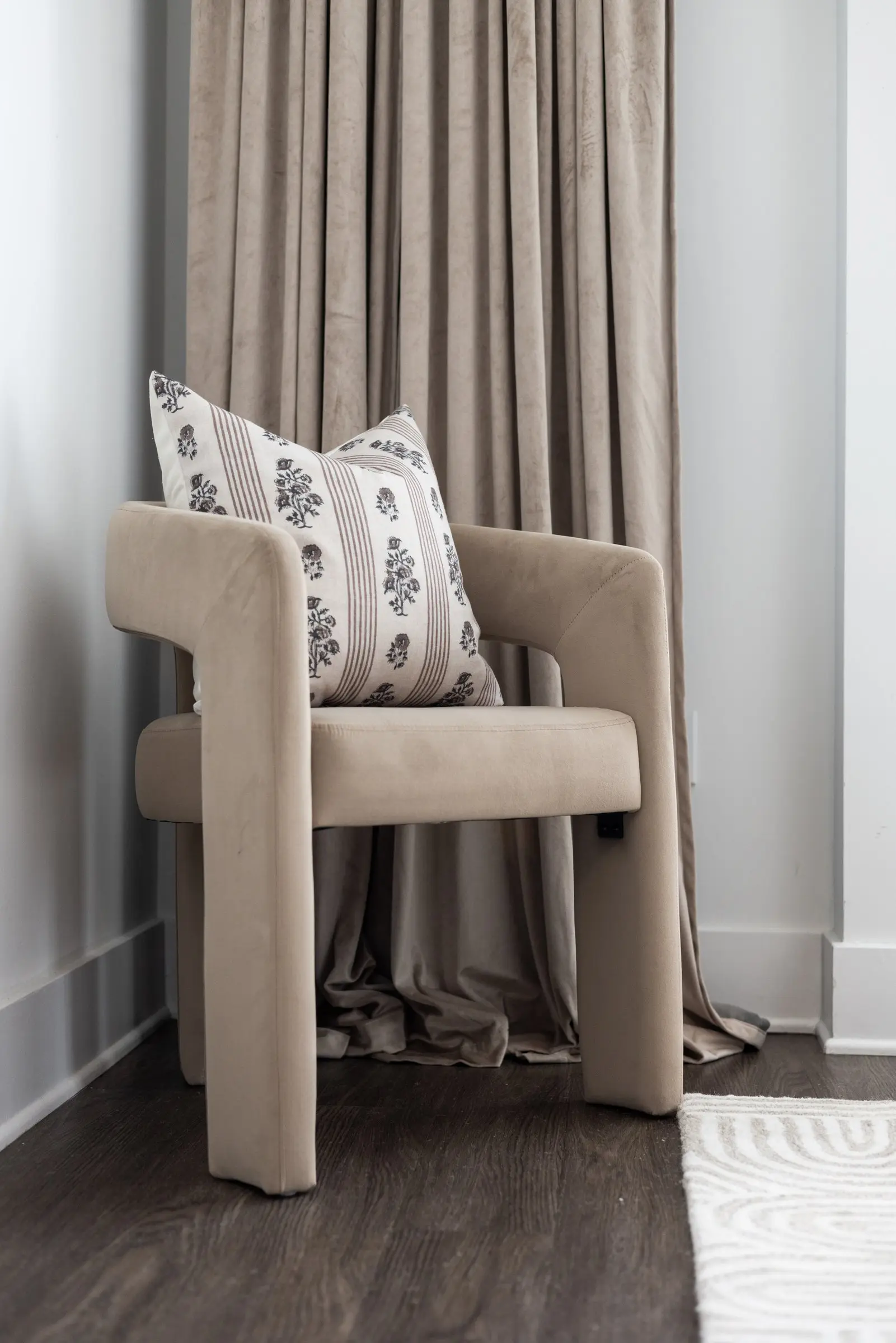 Sculptural taupe chair with a block-print pillow beside linen drapery