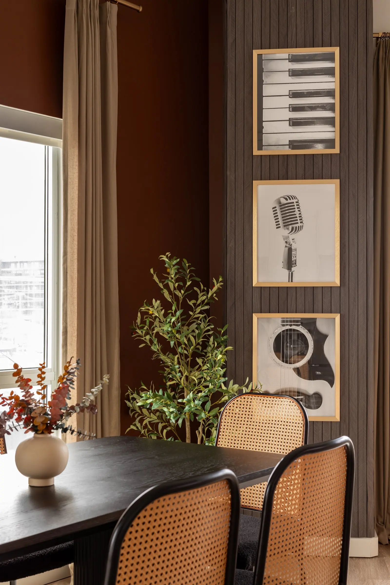 Dining corner with cane chairs, a black table and framed piano, microphone and guitar art on slatted wood paneling