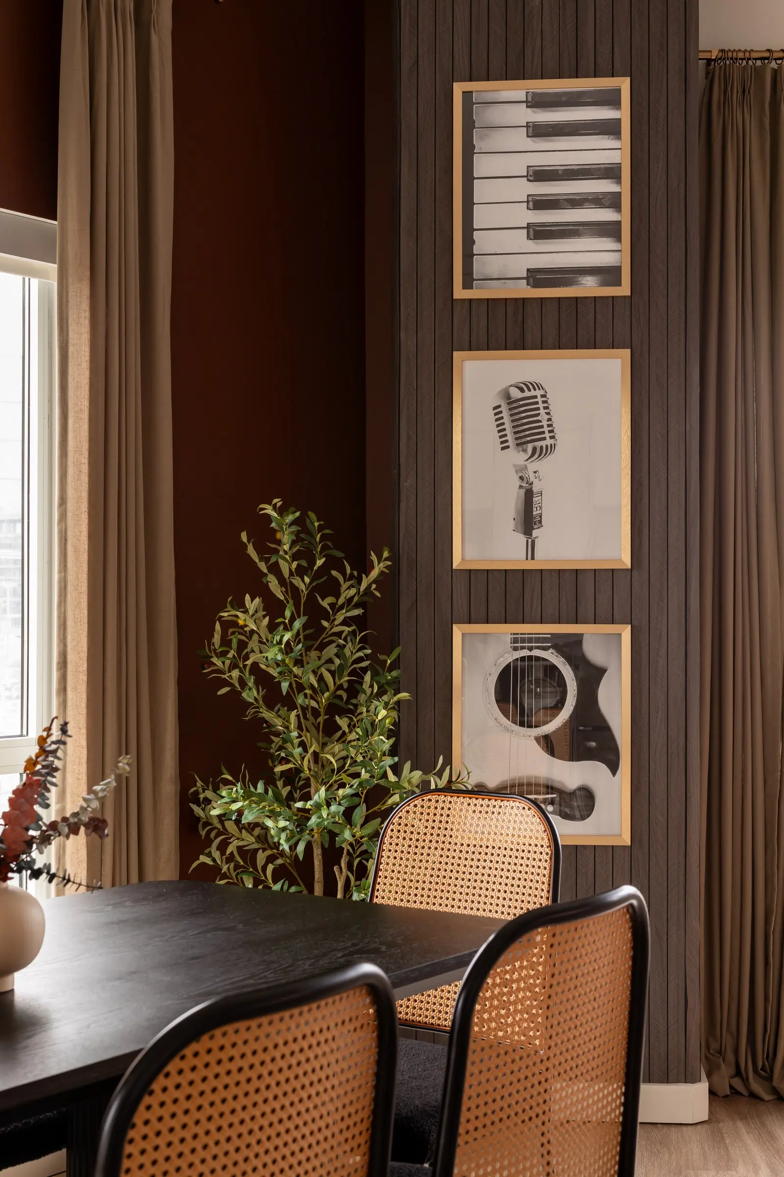 Dining corner with cane chairs and framed piano, microphone and guitar art against rust walls and slatted wood paneling in The Hall of Legends, Nashville