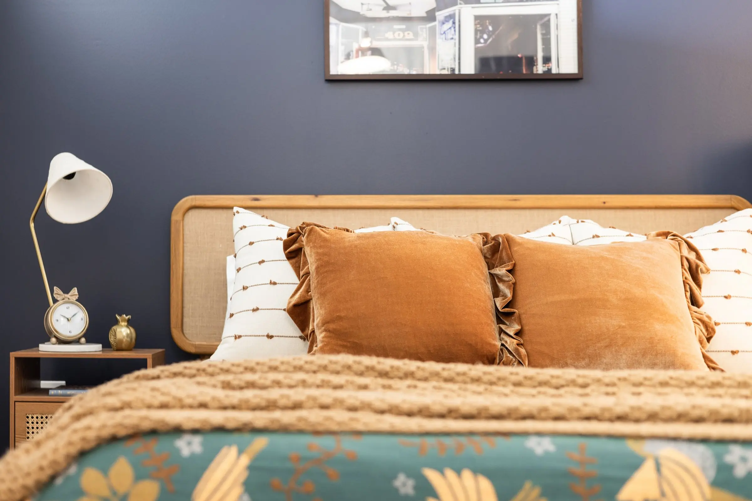 Guest bedroom with navy walls, a woven headboard, rust velvet pillows and a teal floral throw