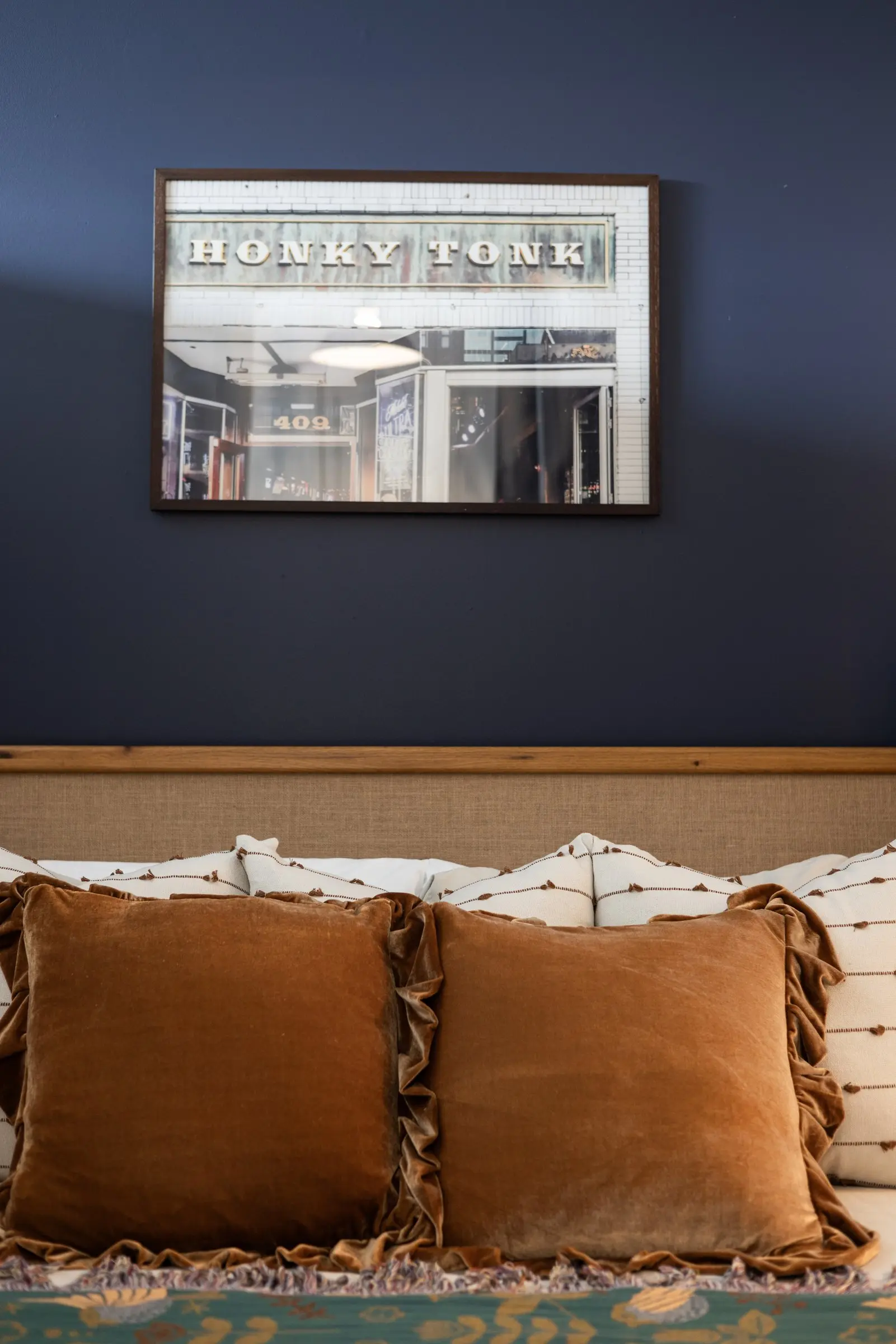 Rust velvet ruffled pillows against a woven headboard under a framed Honky Tonk print