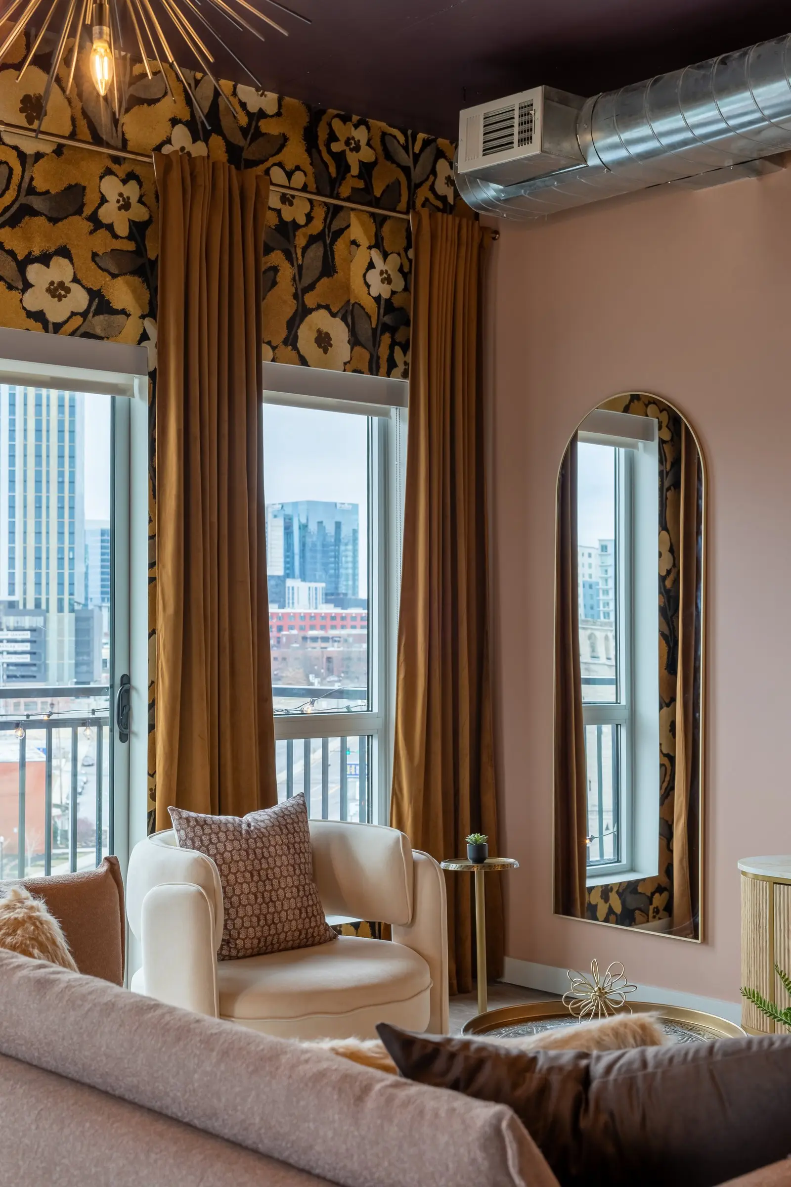Lounge corner with gold floral wallcovering, velvet drapery, an arched mirror and a cream boucle chair